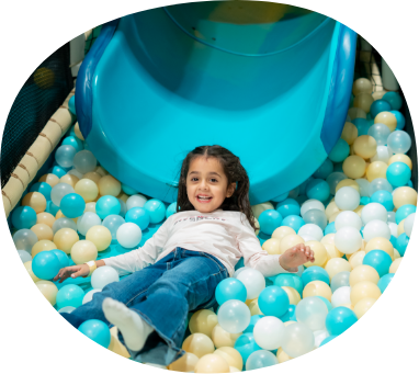 Young child relaxing in pastel ball pit beneath soft play slide at Piccoli.