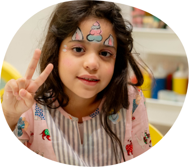 Child with unicorn face paint making peace sign during creative play session at Piccoli.