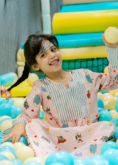 Smiling child with face paint playing in pastel ball pit at Piccoli indoor play area.