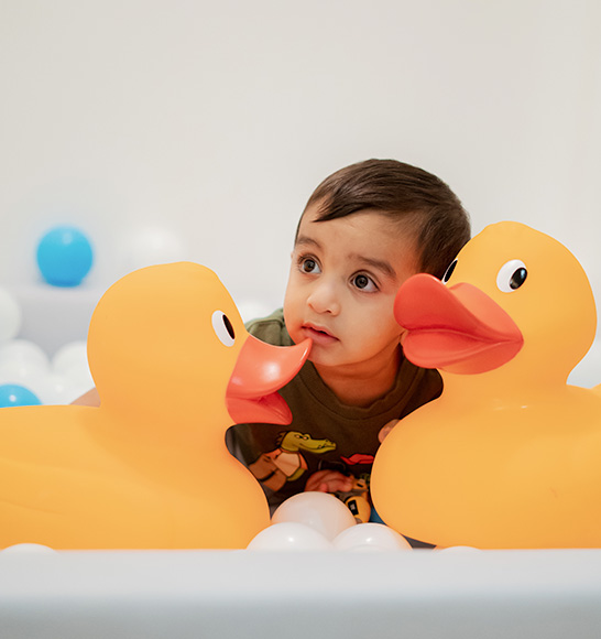 Toddler exploring sensory play with large rubber ducks at Piccoli.