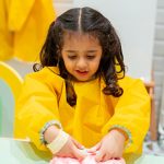 Child wearing yellow apron playing with sensory slime during creative workshop at Piccoli.