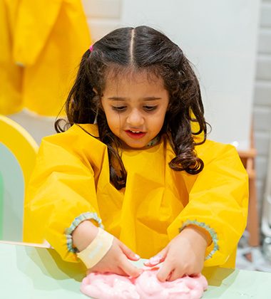 Child wearing yellow apron playing with sensory slime during creative workshop at Piccoli.