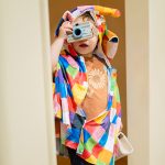 Child dressed in colorful costume pretending to take photos during creative role-play session at Piccoli.