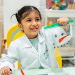 Child in lab coat smiling during hands-on sensory workshop activity at Piccoli creative session.