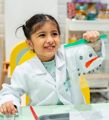 Child in lab coat smiling during hands-on sensory workshop activity at Piccoli creative session.