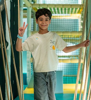 Smiling child giving peace sign while playing in supervised indoor soft play area at Piccoli.